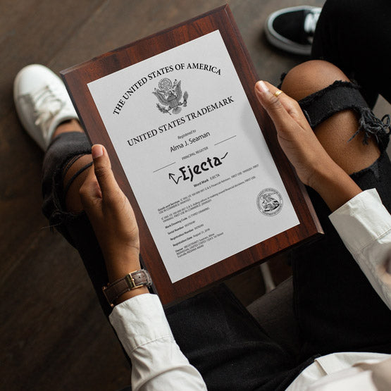 Man In Chair Holding Custom Silver Aluminum Trademark Plaque With Trademark Details And Name On A Wood Board 