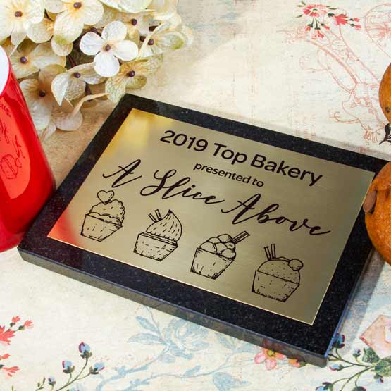 Custom Brass Plaque Award For Top Bakery With Company Name And Logo On Granite Board Sitting On Table With Flowers