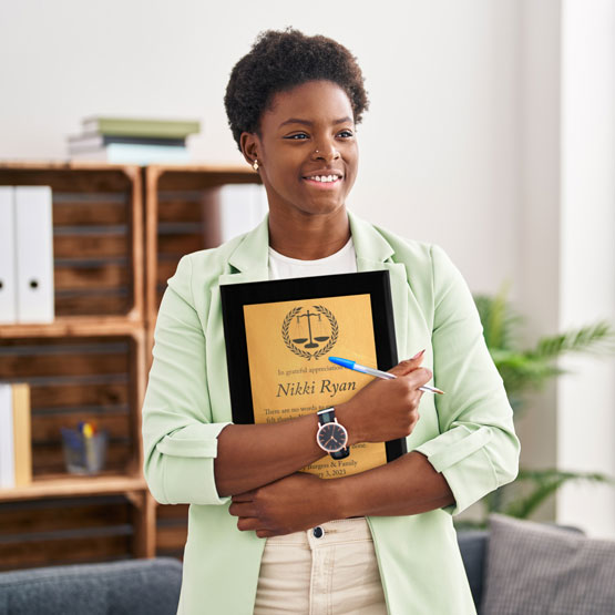 Happy Woman In Office With Couch And Plant Holding A Custom Bronze Appreciation Plaque With Black Board
