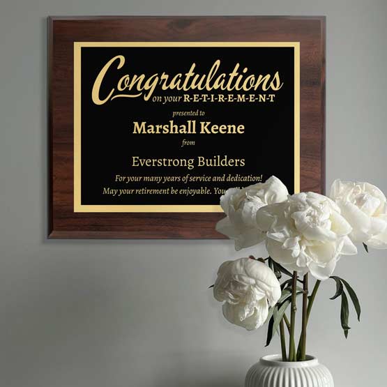 Custom Engraved Congratulations On Your Retirement Plaque On Gray Wall Behind White Roses.