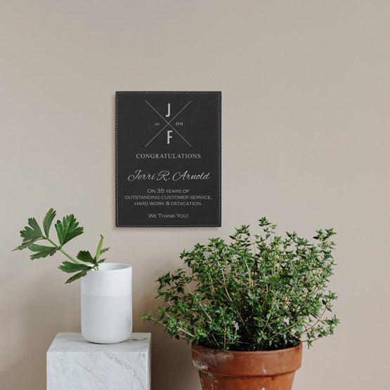 Black Faux Leather Plaque With Logo And Years Of Service Congratulations Message On A Living Room Wall Above Potted Plants
