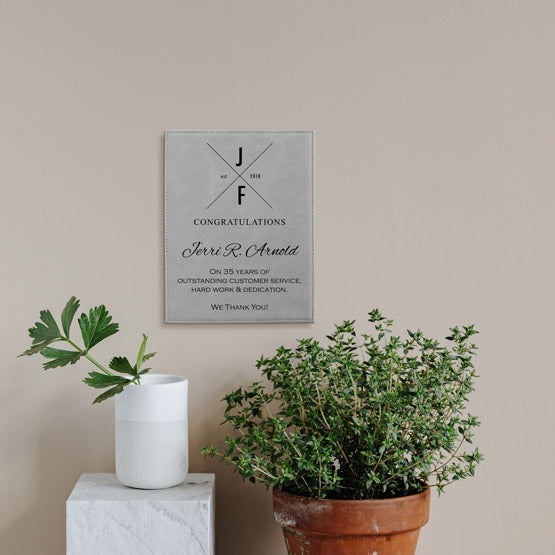 Gray Faux Leather Plaque With Logo And Years Of Service Congratulations Message On A Living Room Wall Above Plants