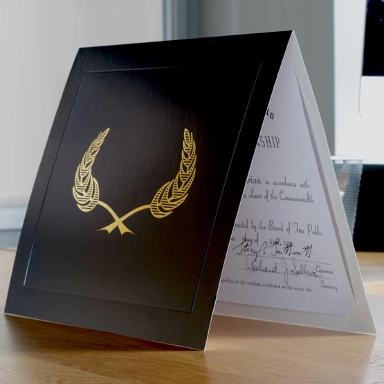 Black Chipboard Presentation Folder With Gold Wheat Art And Slightly Opened To Show Certificate Inside On A Wood Desk