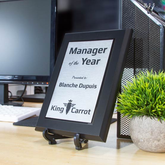Stainless Steel Plaque Award For Manager Of The Year With Black Board And Easel On Office Desk With Plant And Computer