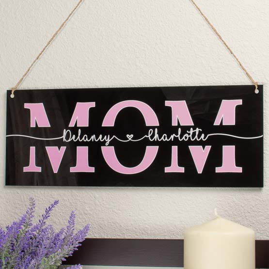 Black Acrylic Sign Printed With Kids Names In Cursive Inside Mom Text Hanging Via Twine Above Shelf With Plant And Candle