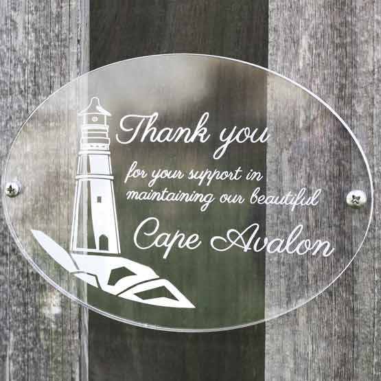 Clear Oval Acrylic Sign With Frosted Engravings Of Lighthouse Art And Appreciation Message Mounted Outdoors On Wood Fence