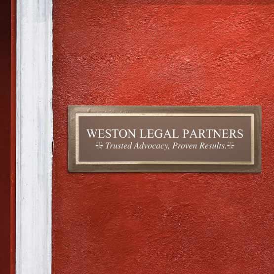 Small Cast Aluminum Sign With Bronze Frame And Brown Plastic Plate Engraved With Law Firm Details And Slogan On Red Wall