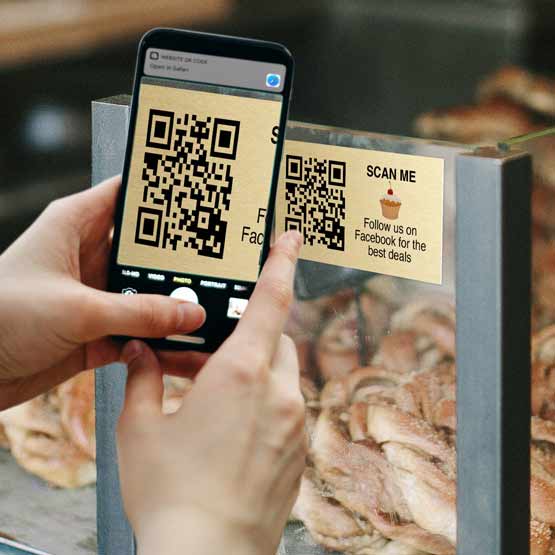 Woman Hands Using Phone To Take Photo Of Gold Aluminum QR Code Tag Printed With Follow Us Message On Glass Bakery Case