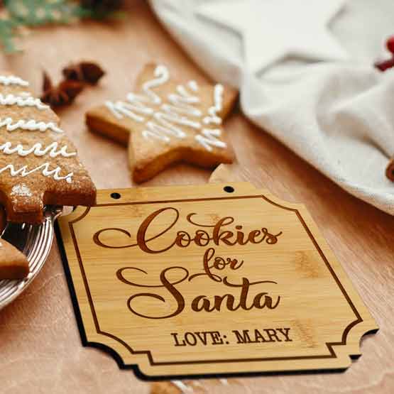 Bamboo Sign With Notched Corners And Engraved With Cursive Cookies For Santa Love Mary Text On Table With Gingerbread Cookies