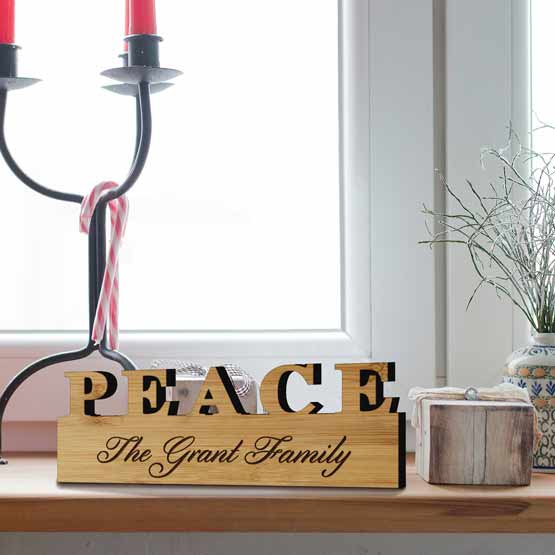 Custom Bamboo Sign With Peace Text Cutout And Engraved With The Grant Family Text On Wood Shelf With Holiday Decor