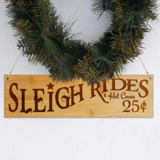 Bamboo Sign Engraved With Sleigh Rides And Hot Cocoa And Twenty-Five Cents Message Hanging Under Wreath Via Twine