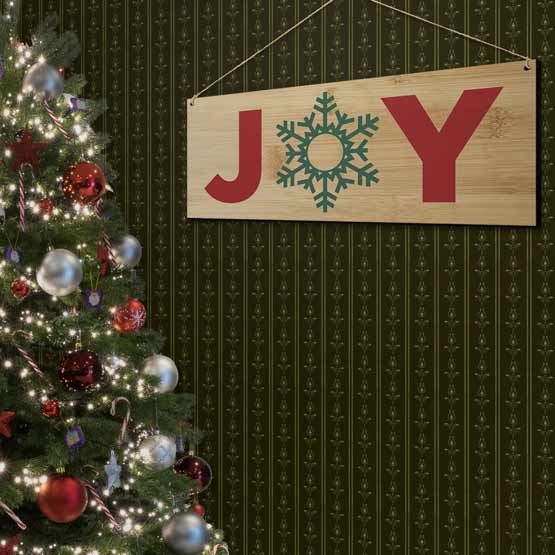 Full Color Bamboo Sign Printed With Snowflake Art Inside Joy Text Hanging On Living Room Wall Via Twine Near Christmas Tree