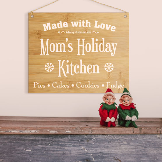 Full Color Bamboo Sign Printed With Mom’s Holiday Kitchen Message Hanging Via Twine Above Shelf With Festive Elf Figures