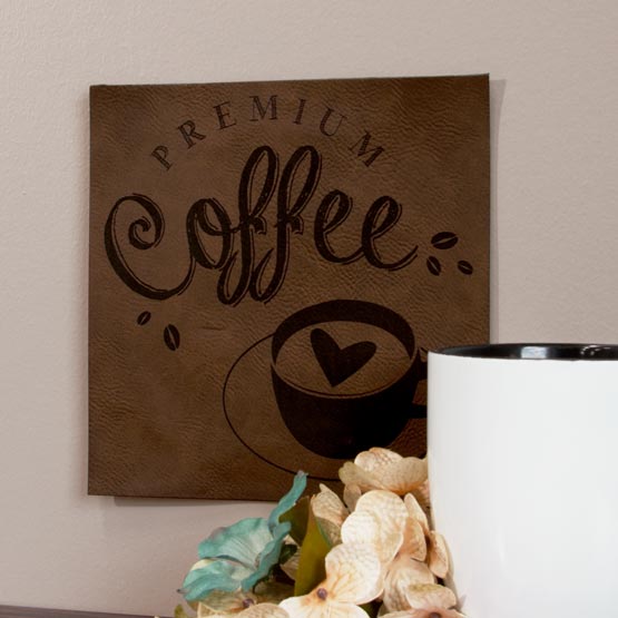 Dark Brown And Black Faux Leather Sign Engraved With Premium Coffee Logo On Wall Above Shelf With Flowers And Coffee Mug