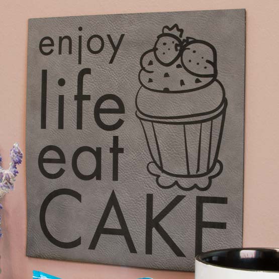 Gray And Black Faux Leather Sign Engraved With Cupcake Art And Enjoy Life Eat Cake Text Mounted On Wall Near Coffee Mug