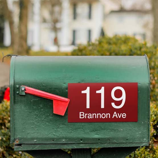 Red Plastic Address Sign Laser Engraved With Address Details Mounted Outdoors On Green Mailbox Near Lowered Mailbox Flag