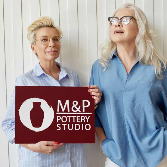 Two Older Women Outside House Holding Custom Red Plastic Ships Today Sign Laser Engraved With Pottery Studio Logo