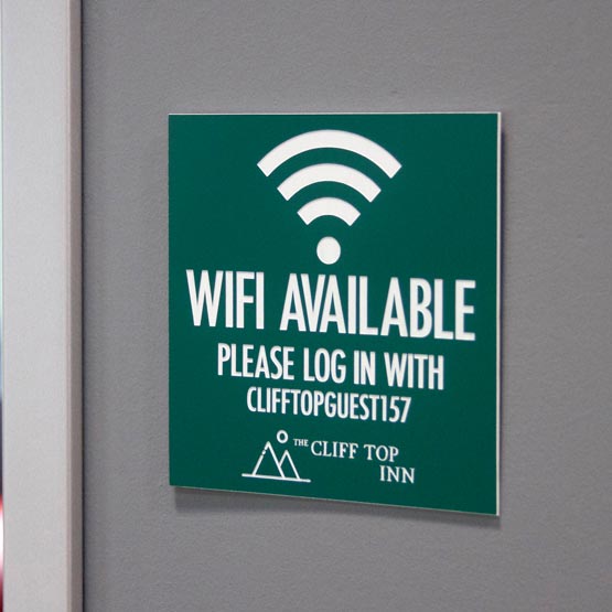 Green Plastic WiFi Sign Engraved With WiFi Icon And Login Details And Company Logo Mounted On Gray Office Wall