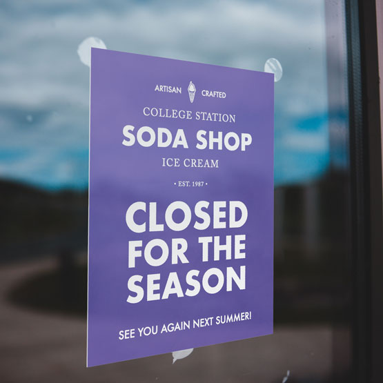 Blue Plastic Sign Engraved With Soda Shop Details And Closed For The Season Message Mounted On Glass Window Via Suction Cups