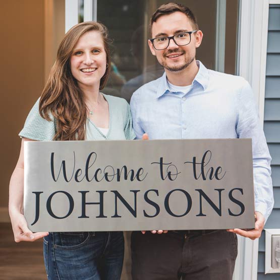 Couple On Front Porch Holding Custom Stainless Steel Sign Laser Fused With Welcome To The Johnsons Message